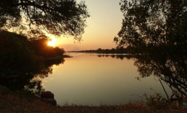 a body of water with trees around it and a sunset